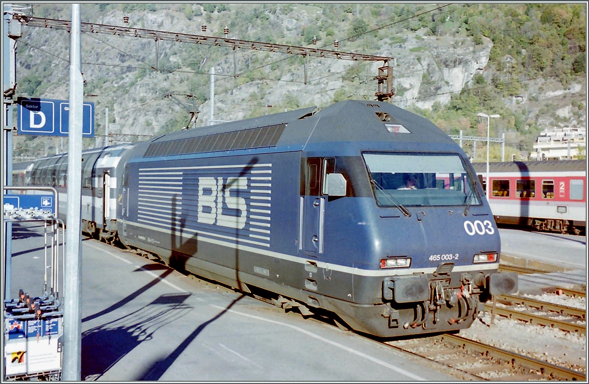 Die relativ bildfüllende BLS Re 465 003-2 mag zwar das Motiv des Bildes sein, grund für das zeigen sind aber die vielen Details rumherum: da wäre einersteits die Tasache, dass die Lok eine Reisezug zeiht, und zwar eine EC nach Milano, der damals über einen Panoramwagen verfügte, dann wäre vieleicht auch noch die alte Fahrleitungsanlage zu erwähne, sowie rechts im Bild die DB EC Wagen, die wohl als EC  Lötschberg  auf ihre Abfahrt warten.
Das Analogbild entstand im Oktober 1995