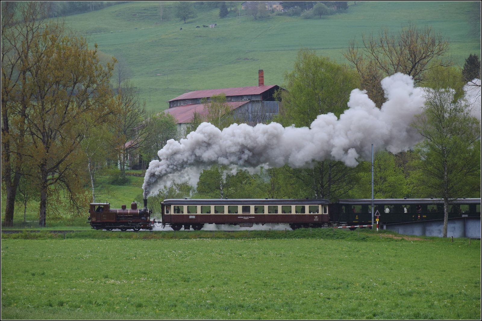 Vapeur Val-de-Travers: Train  Au fil de l'Areuse .

E 3/3 8511 nimmt mit Getöse schon beim ehemaligen Asphaltwerk in La Presta Anlauf für die Steigung nach Travers. Mai 2023.