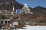 Der SSIF Treno Panoramico Vision Vigezzo vor der Kulise der Wahlfahrtskirche  Madonna del Sangue  in Re.